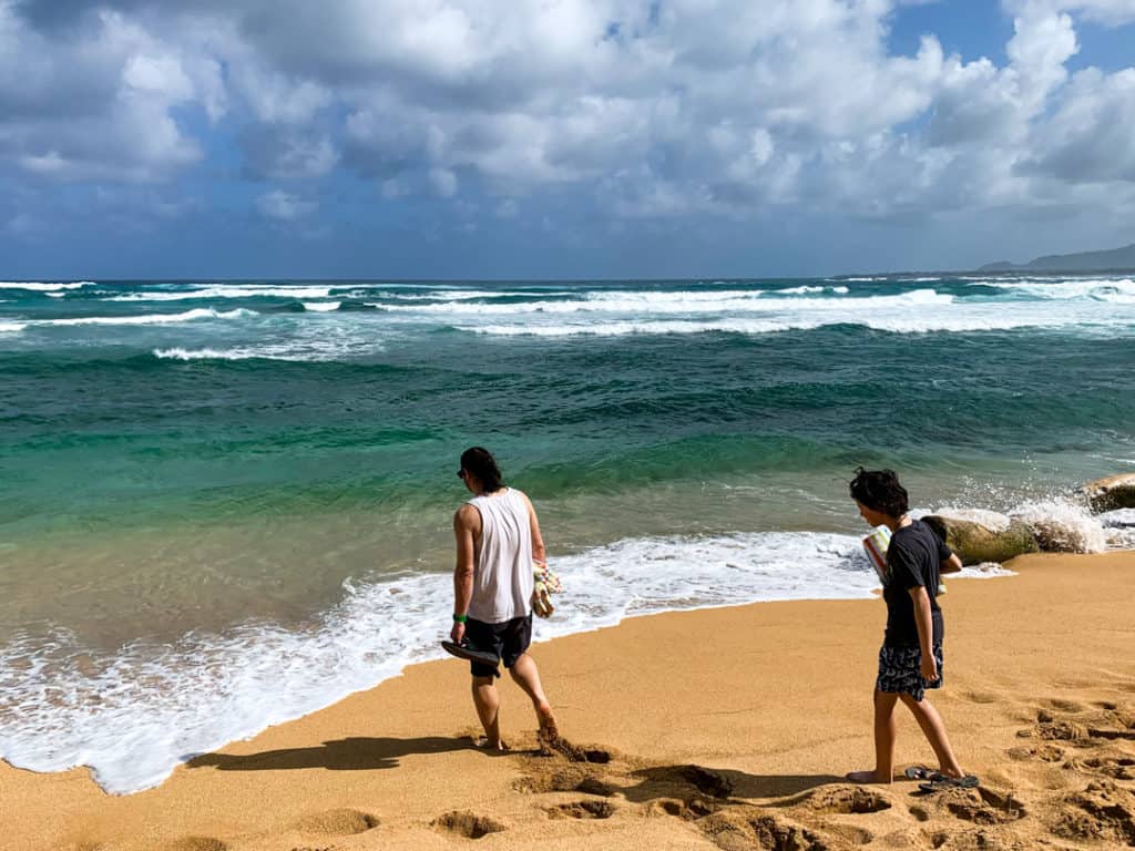 Father and son walking towards aqua water on Kauai beach