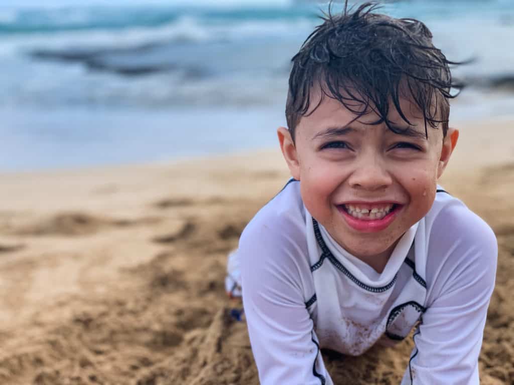 Boy smiling with wet hair and laying in sand on beach