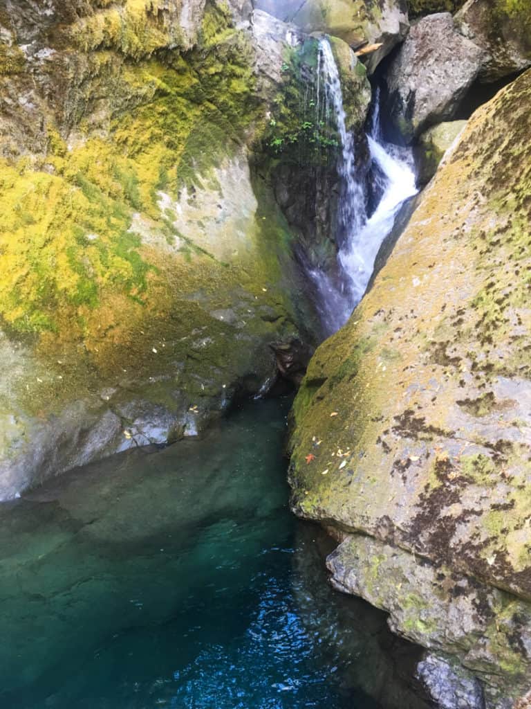 waterfall spilling between two large mossy boulders into clear teal colored water below