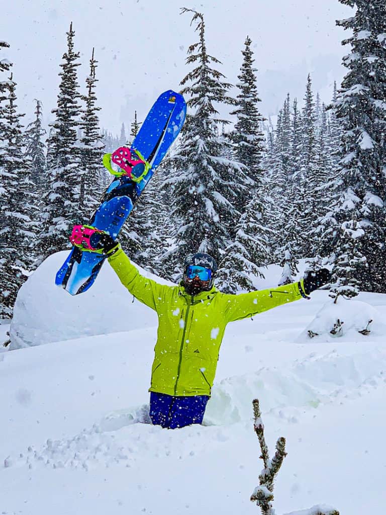 man standing in deep powder holding LibTech Orca snowboard up in air