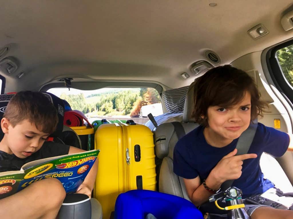 Two boys in van on road trip, one looking at hotwheels coloring