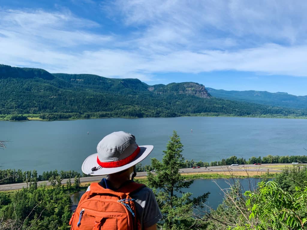 boy wearing sun hat and backpack looking out over the Columbia River Gorge during a hike