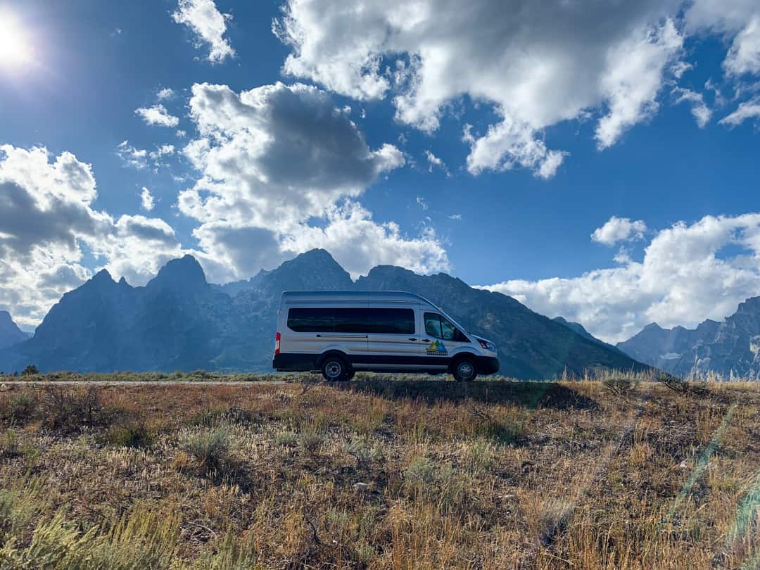 campervan framed by Teton mountain range under blue skies with white clouds