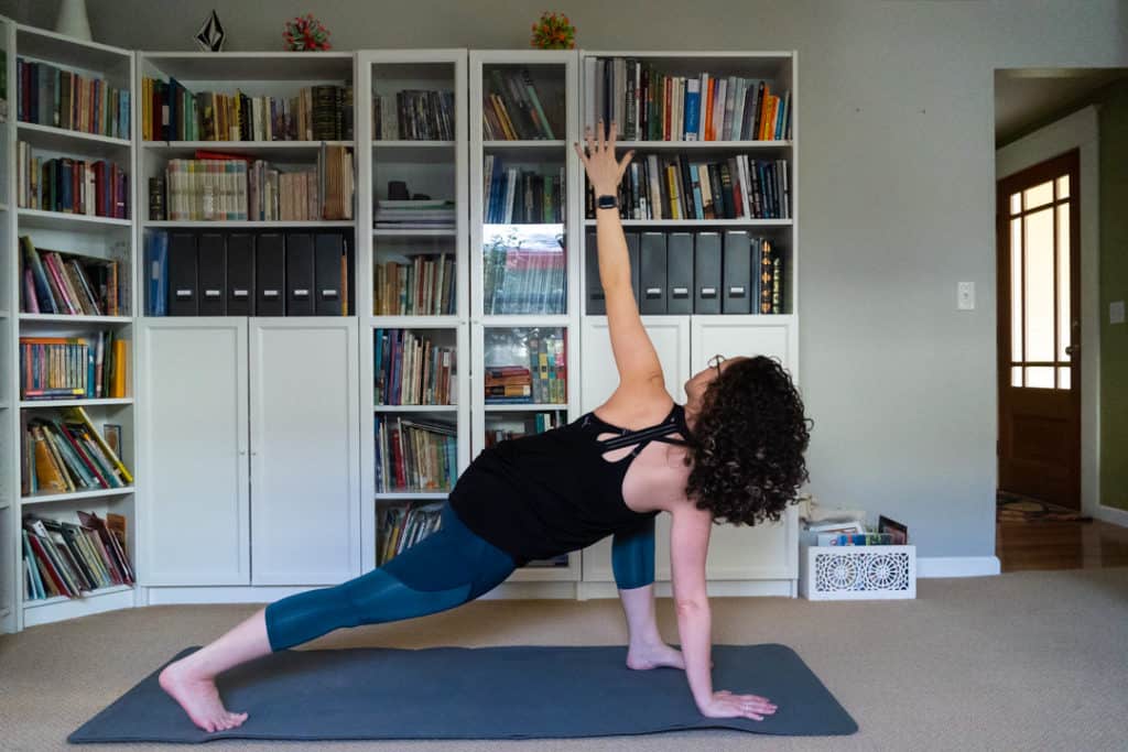 woman in black tank and teal yoga pants doing yoga pose in front of white bookcases
