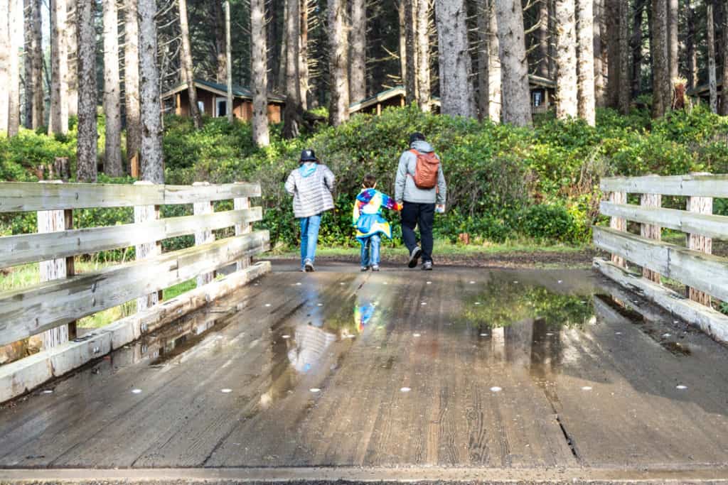 father and two sons walking across bridge towards state park cabins nestled among the forest