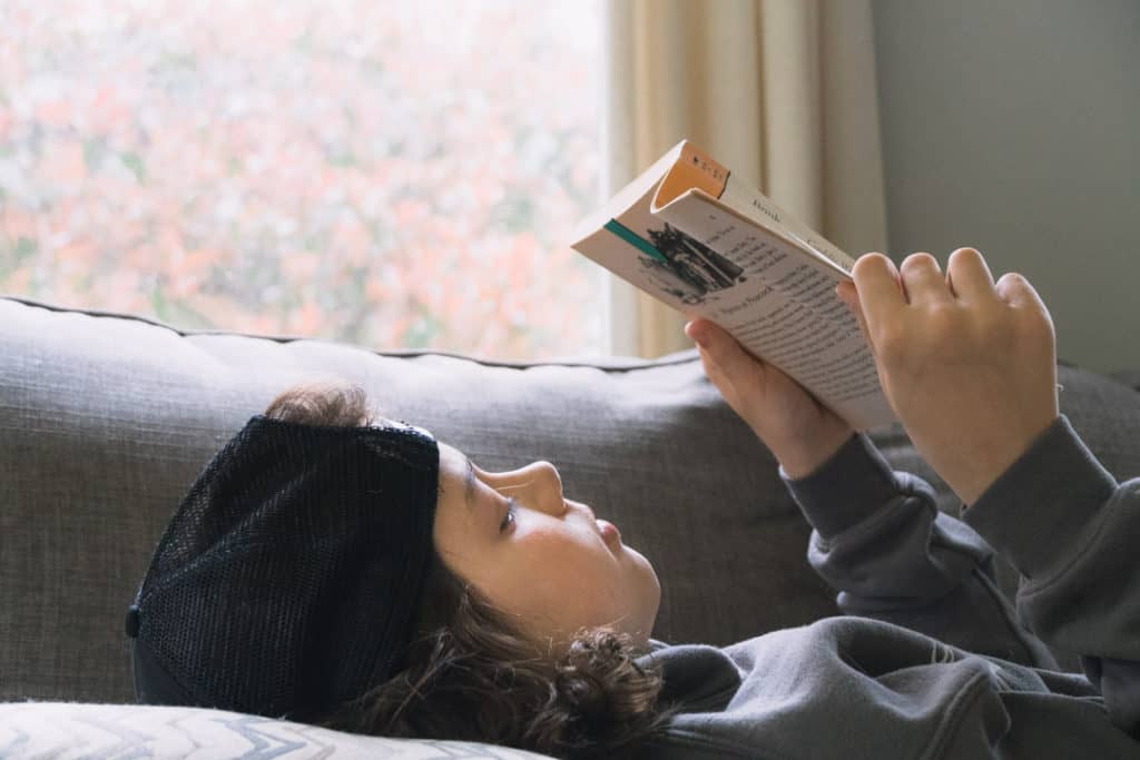 boy reading a living book while laying on couch in front of a window