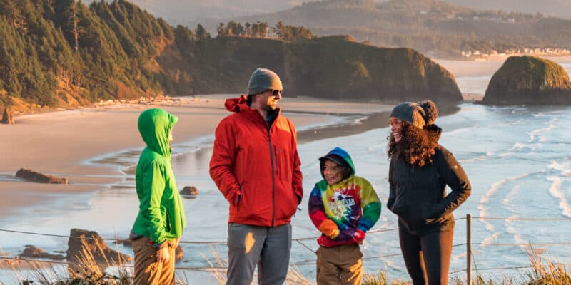 family of four posing with the ocean in the distance and cannon beach coastline behind them with golden hour colors