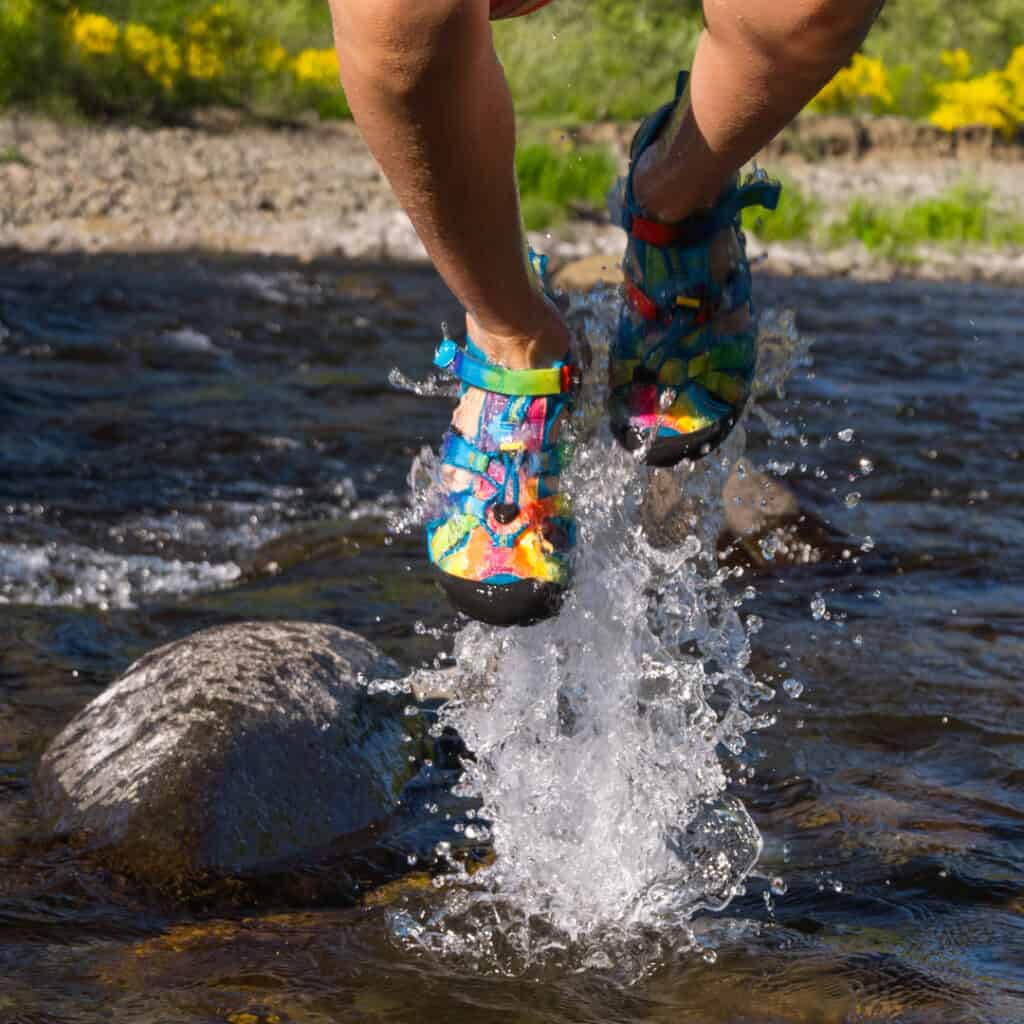 image of kid jumping in river wearing KEEN sandals in tie-dye on a sunny day