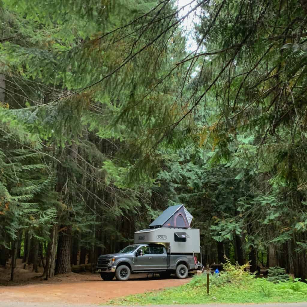 Scout Kenai on F350 Tremor set up with rooftop tent in use at campsite in the Pacific Northwest under evergreen trees 