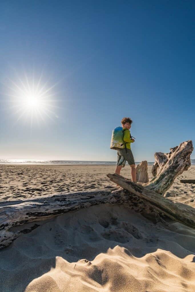 boy wearing icemule jaunt backpack stands on top of driftwood at the oregon coast