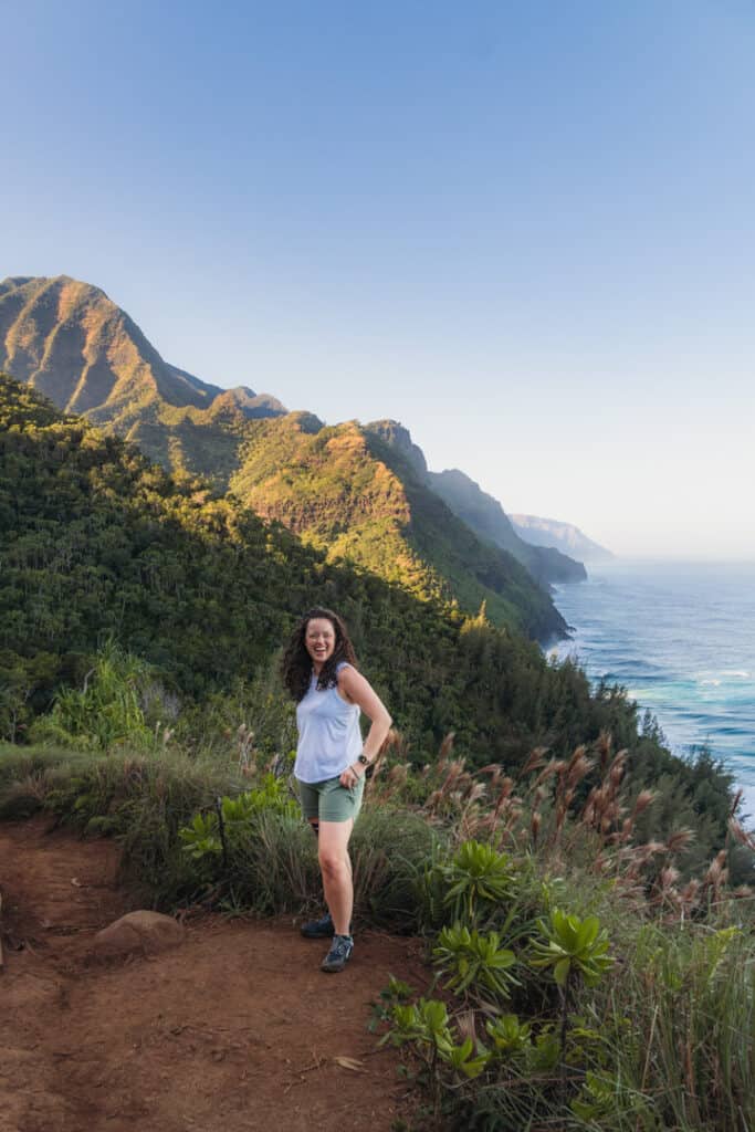 woman stands in front of Napali Coastline along the Kalalau Trail