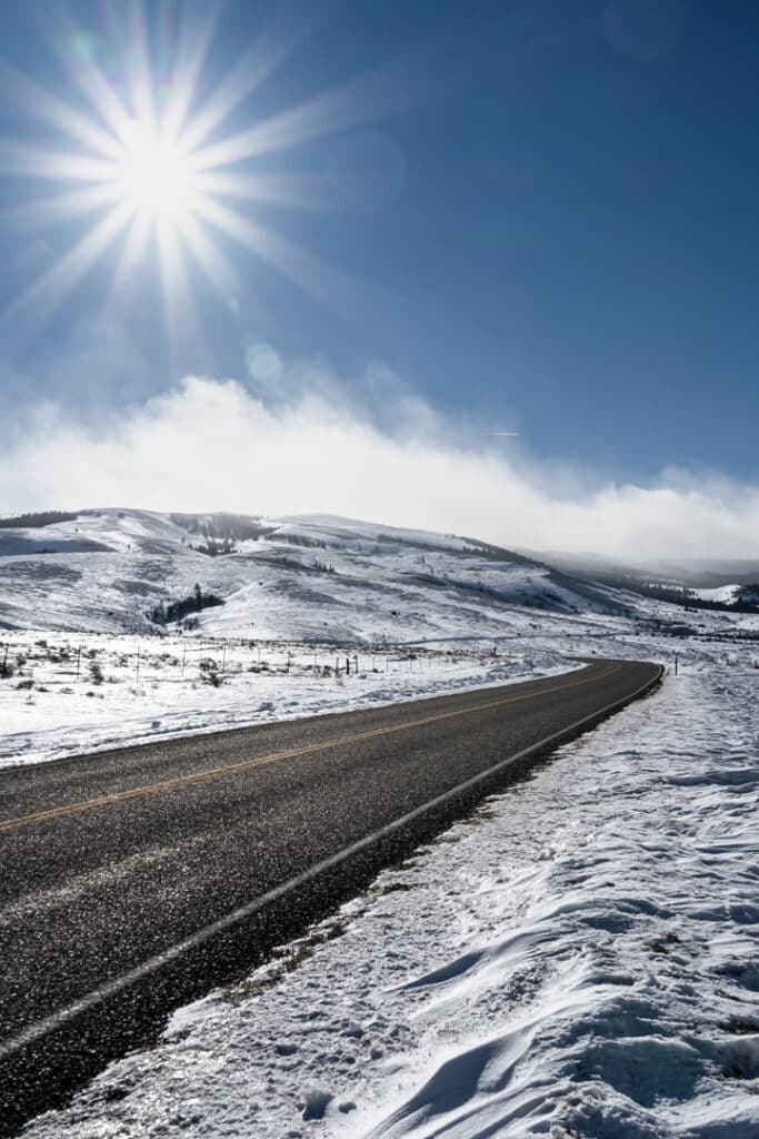 road winds into distance among snowy landscape under blue skies with sunburst