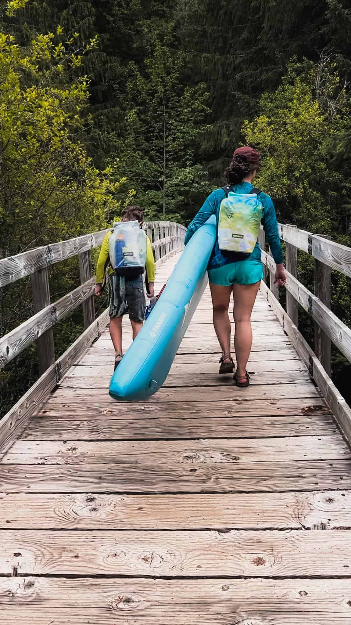 mother and son cross bridge with backpack coolers and mom carrying paddleboard