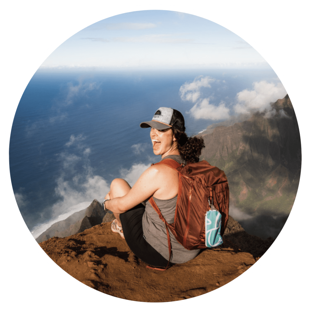 woman sits smiling at edge of cliff along Kauai coastline