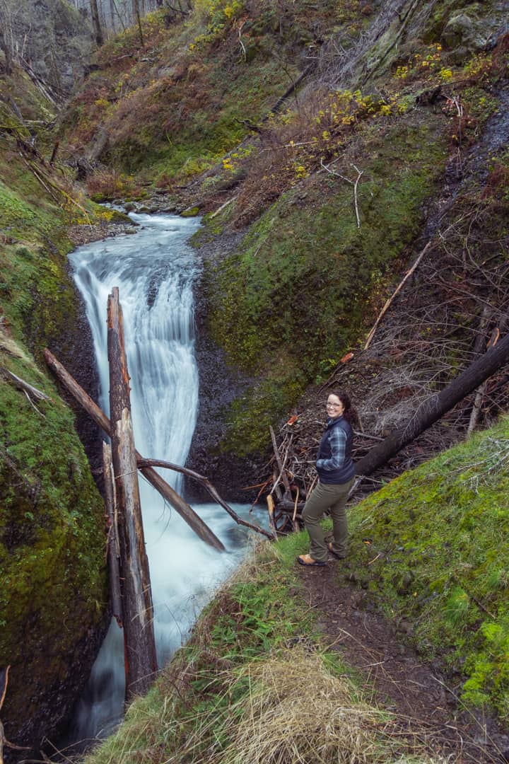 woman looks over shoulder next to waterfall in Columbia River Gorge
