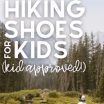 boy stands on rock looking at grand tetons with text overlay that says 13+ of the best hiking shoes for kids (kid approved)