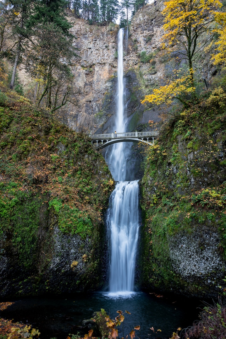double tiered waterfall flows under bridge among fall colors