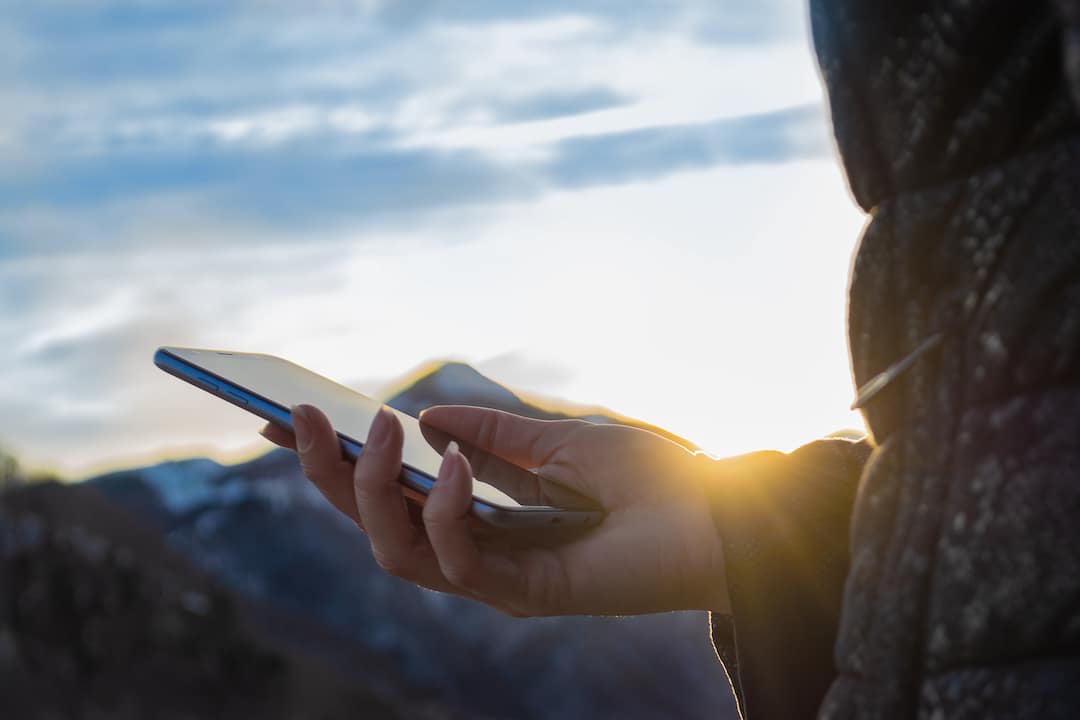 Person holds cell phone while camping in hand at sunset with mountains in the distance.