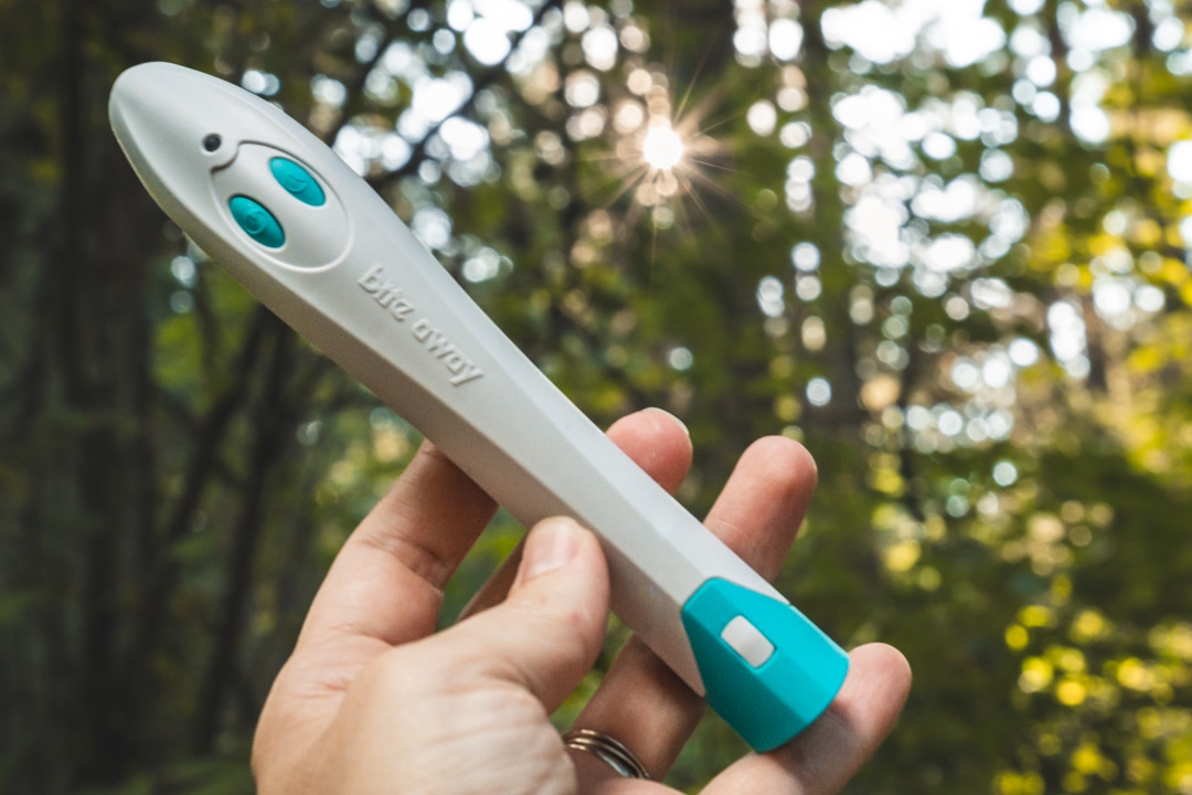 hand hold bite away up in front of green trees and sunburst to show details of the device including two buttons for treatment lengths of 3-5 seconds and size of device